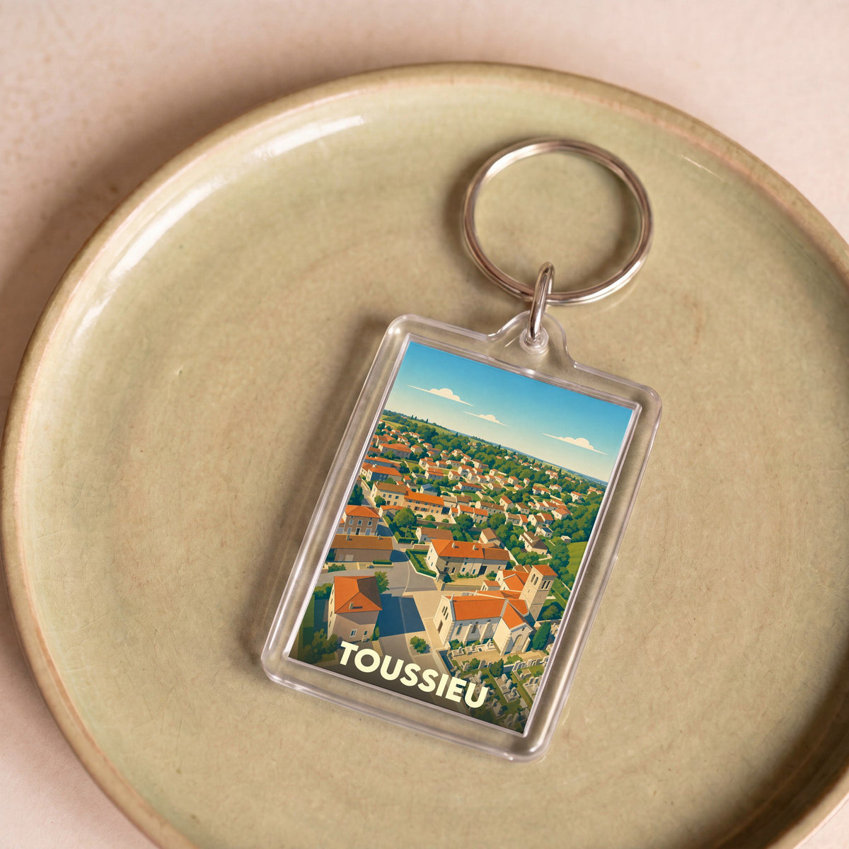 Porte-clés souvenir de la ville de Toussieu avec une illustration stylisée d'un paysage urbain vue du ciel.