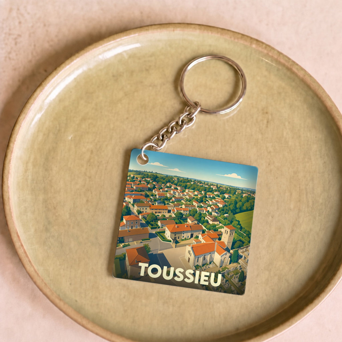 Porte-clés souvenir de la ville de Toussieu avec une illustration stylisée d'un paysage urbain vue du ciel.