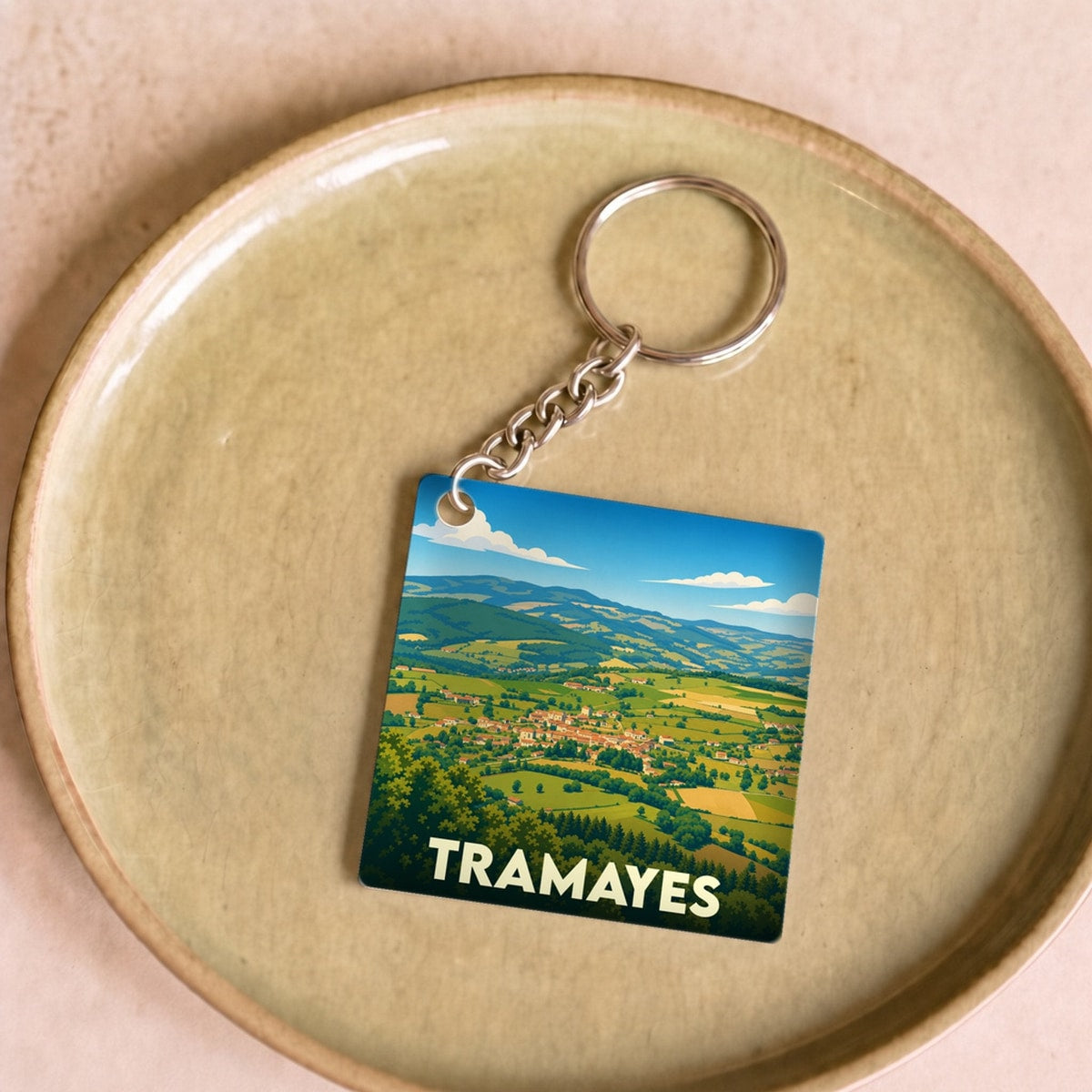 Porte-clés souvenir de la ville de Tramayes avec une illustration paysagère stylisée.