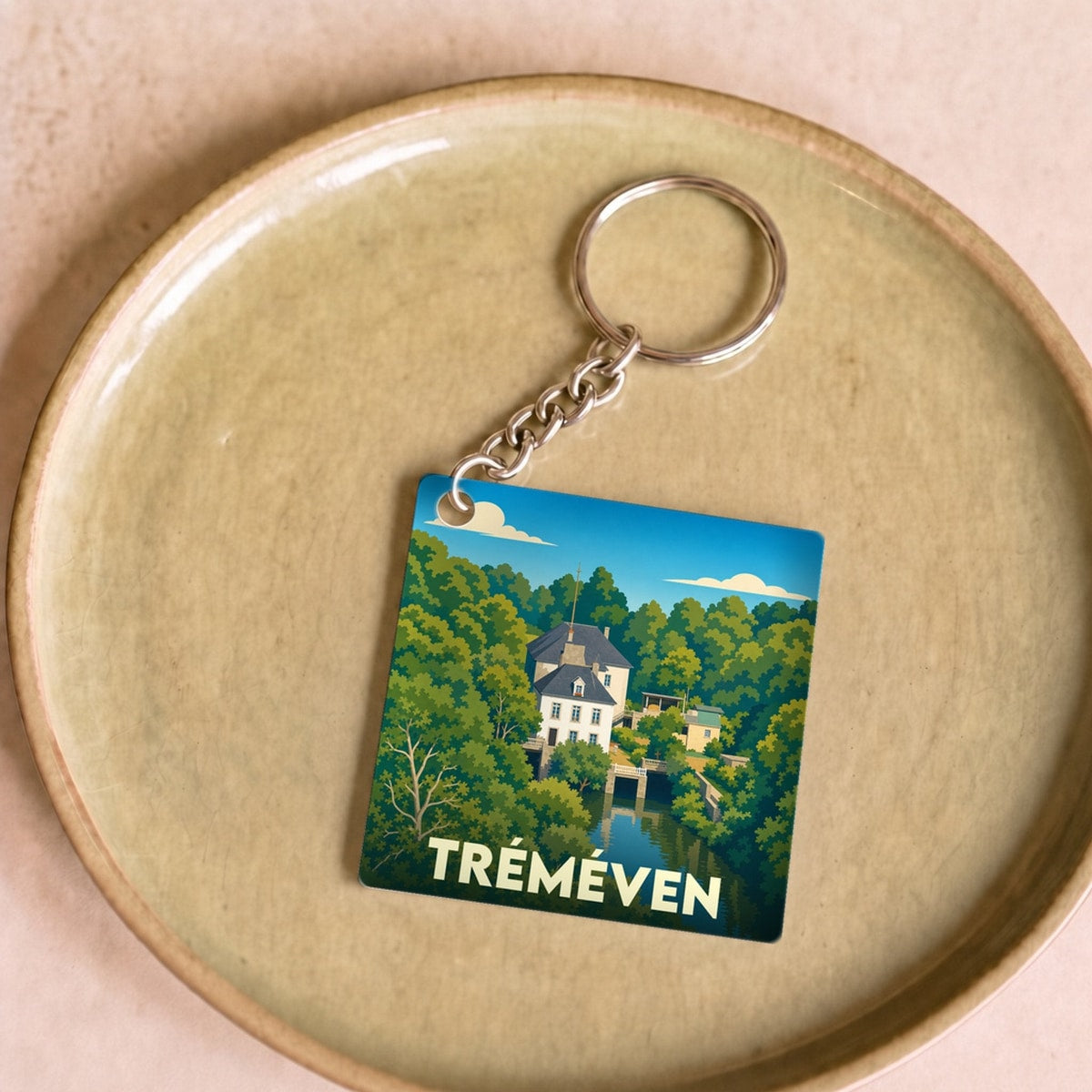 Porte-clés souvenir de la ville de Tréméven avec une illustration stylisée d'un manoir au bord de l'eau.