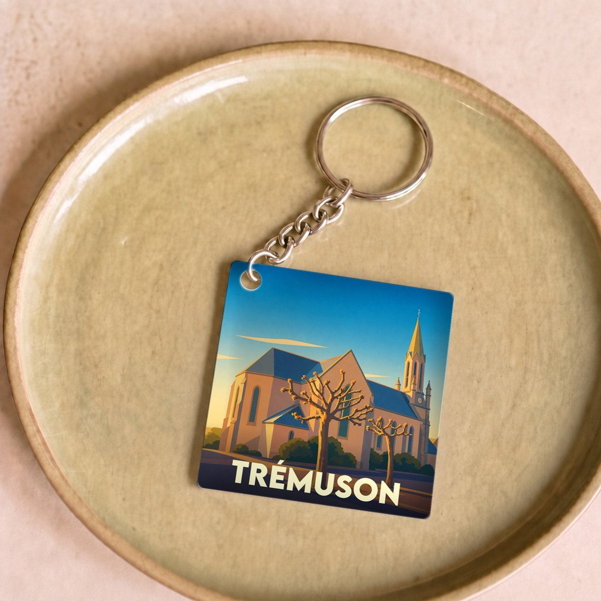 Porte-clés souvenir de la ville de Trémuson avec une illustration stylisée de son église au coucher du soleil.