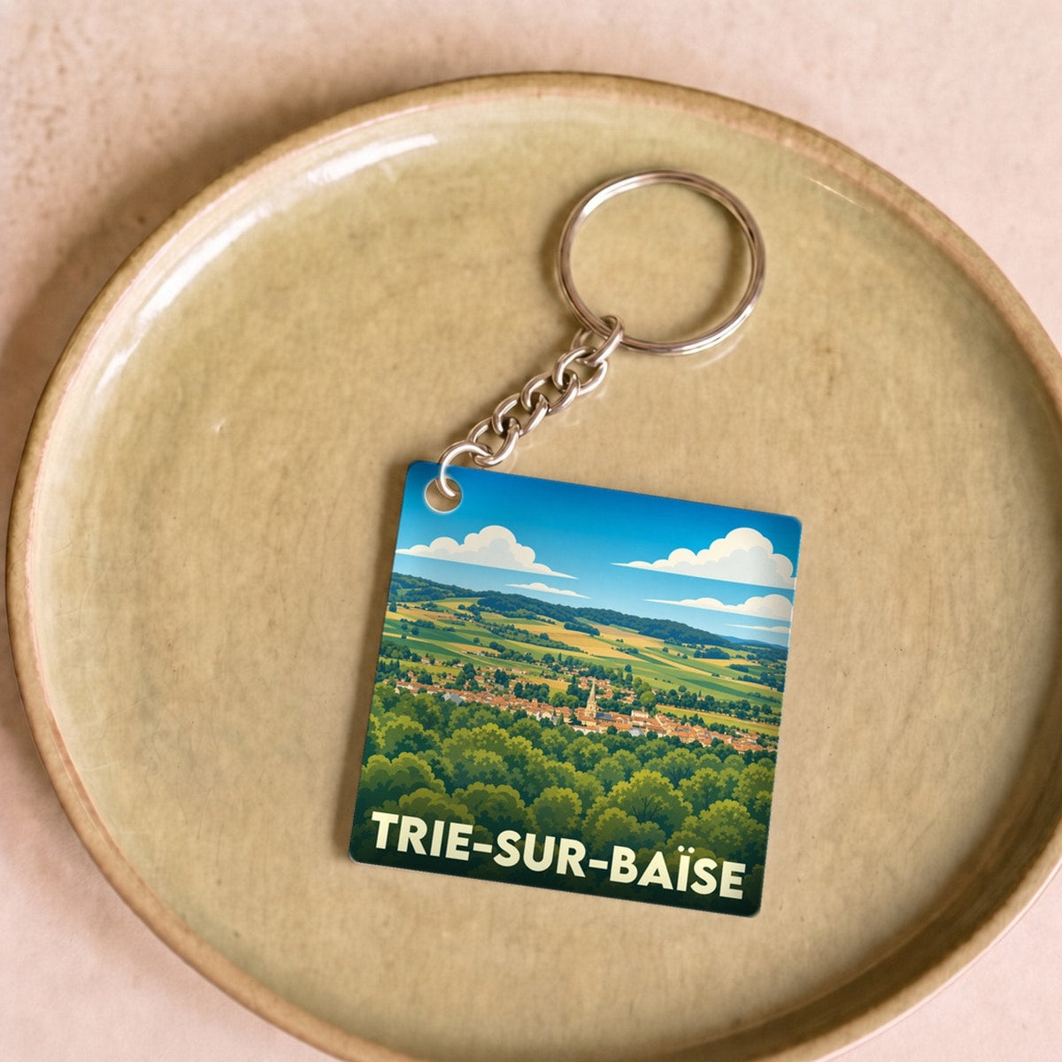 Porte-clés souvenir de la ville de Trie-sur-Baïse avec une illustration stylisée de son paysage.