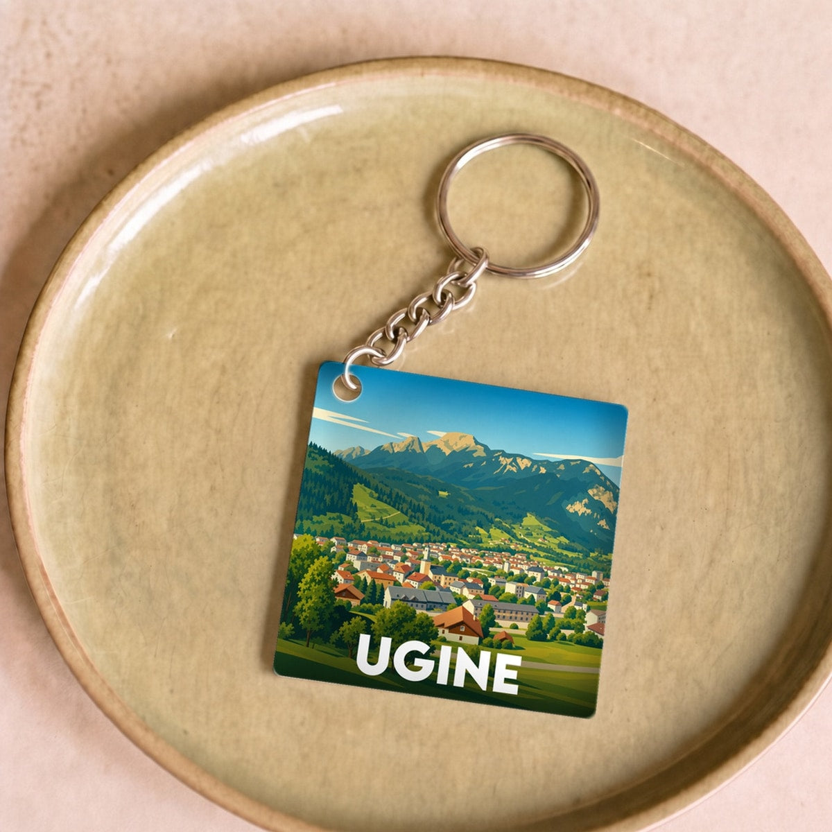 Porte-clés souvenir de la ville d'Ugine avec une illustration stylisée d'un paysage montagneux.