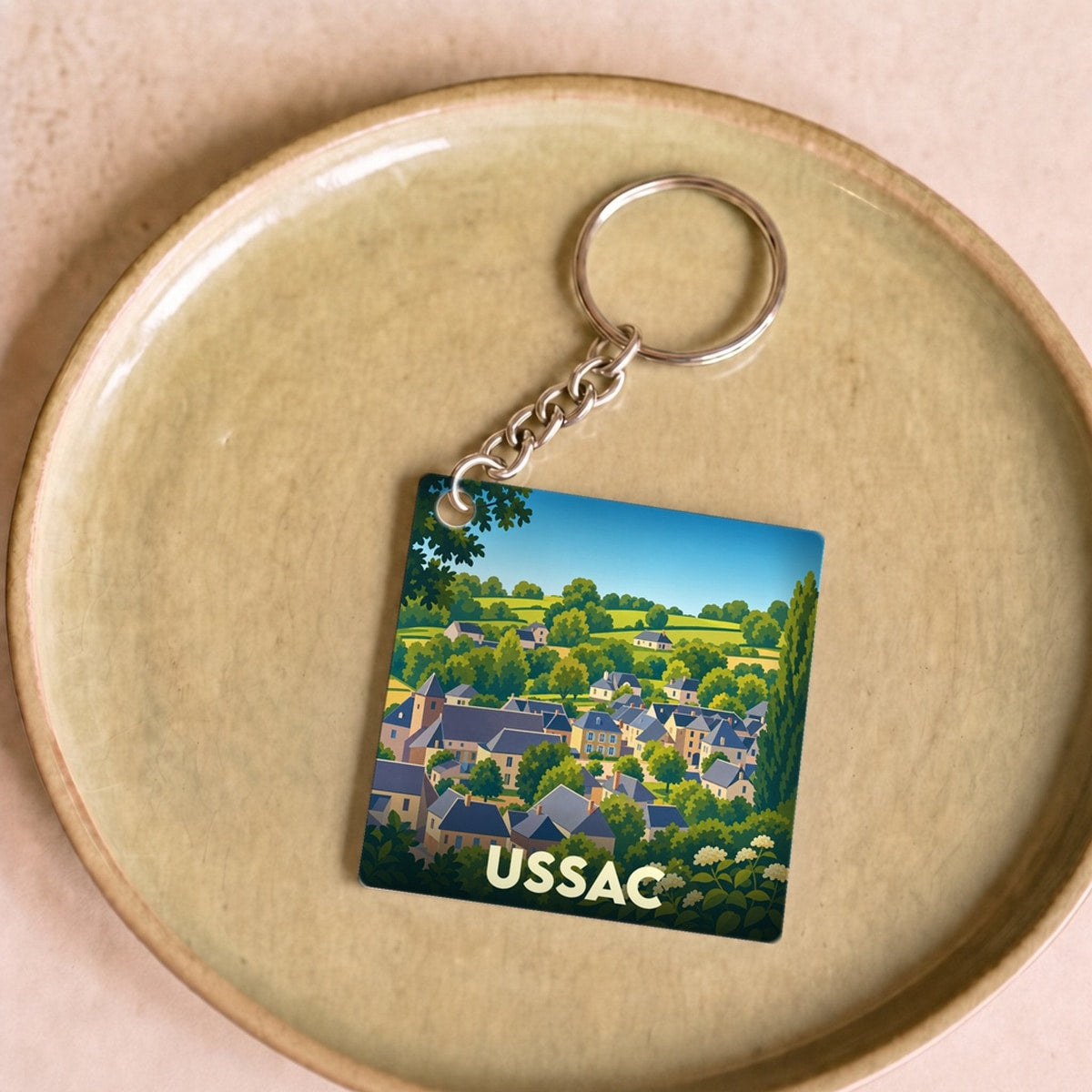 Porte-clés souvenir de la ville d'Ussac avec une illustration stylisée de ses paysages et habitations.