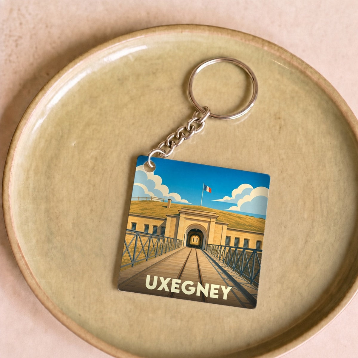 Porte-clés souvenir de la ville d'Uxegney avec une illustration stylisée de son fort historique.