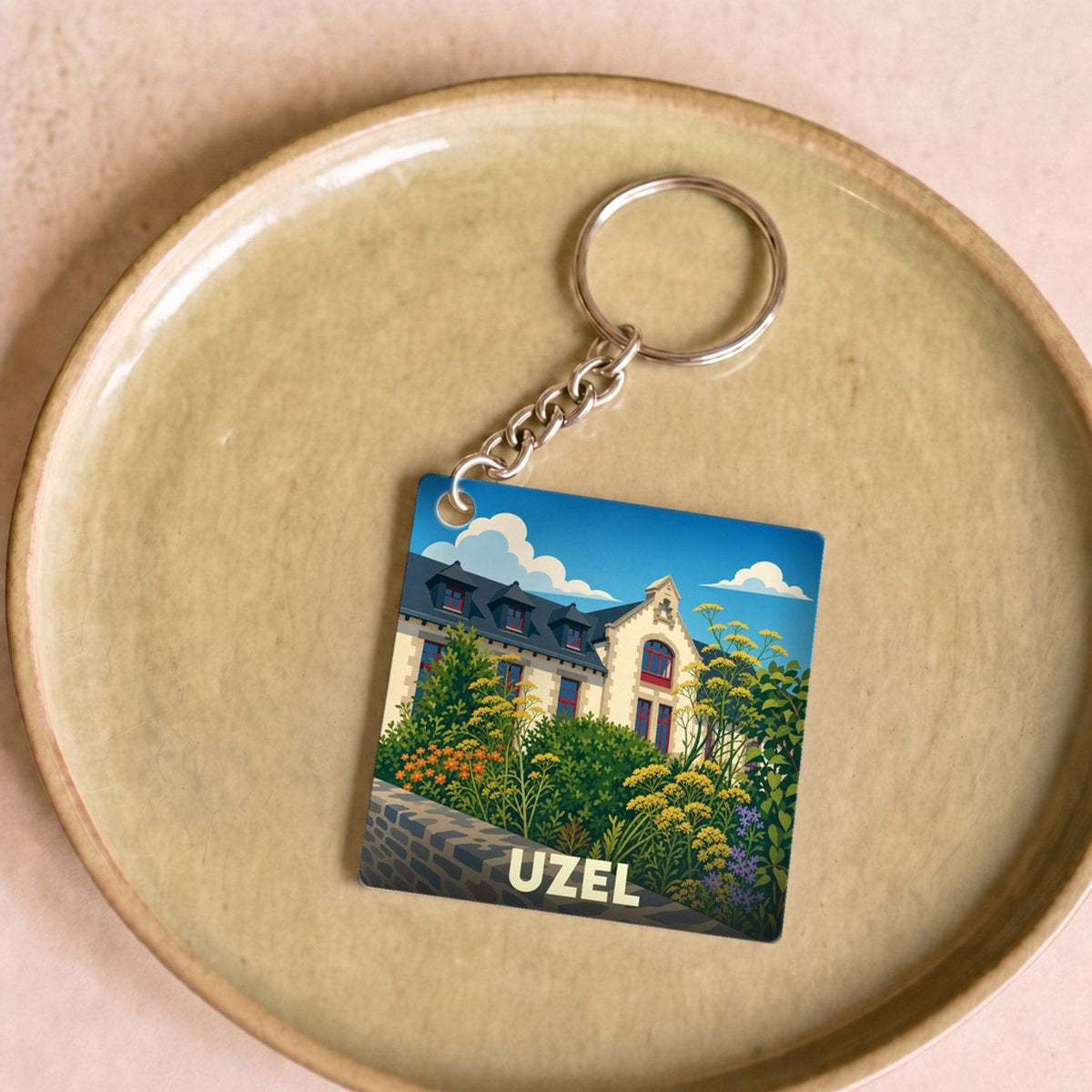 Porte-clés souvenir de la ville d'Uzel avec une illustration stylisée d'un bâtiment fleuri.