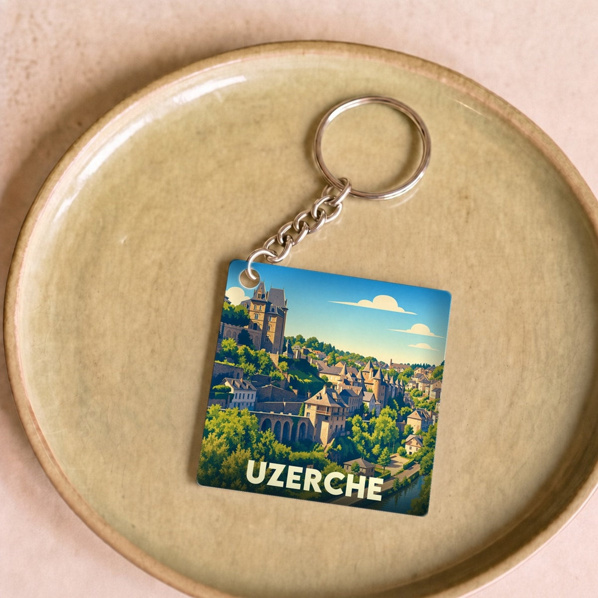 Porte-clés souvenir de la ville d'Uzerche avec une illustration stylisée de ses bâtiments historiques et de sa rivière.