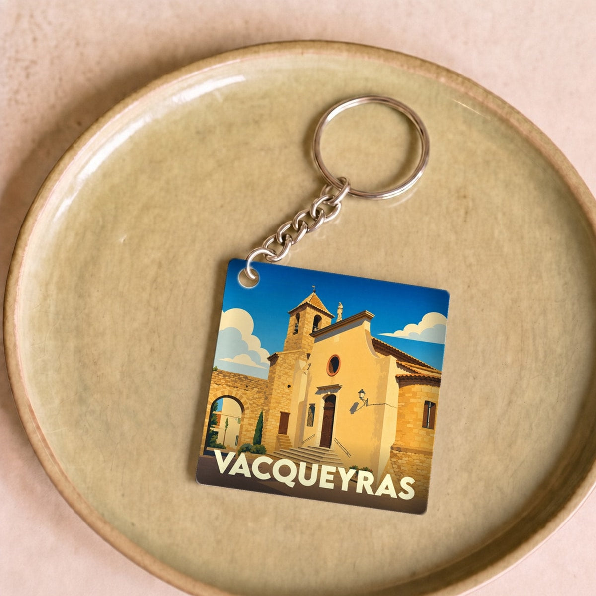Porte-clés souvenir de la ville de Vacqueyras avec une illustration stylisée de l'église locale sous un ciel bleu.