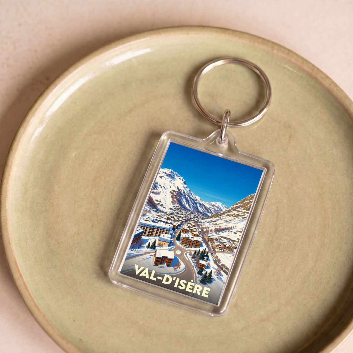 Porte-clés souvenir de Val-d'Isère avec une illustration montrant le village enneigé au pied des montagnes.