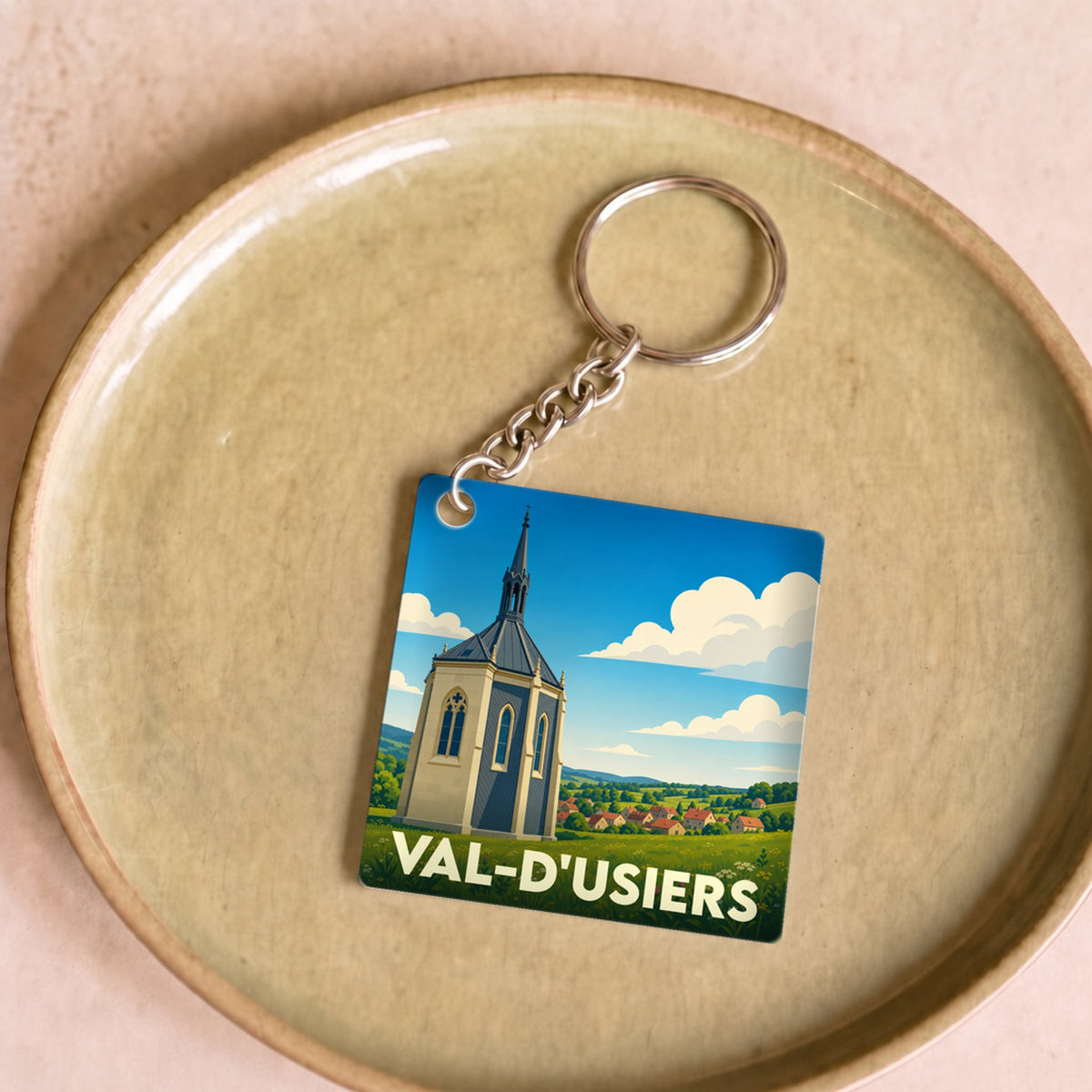 Porte-clés souvenir de Val-d'Usiers avec une illustration stylisée d'une chapelle dans un paysage verdoyant.