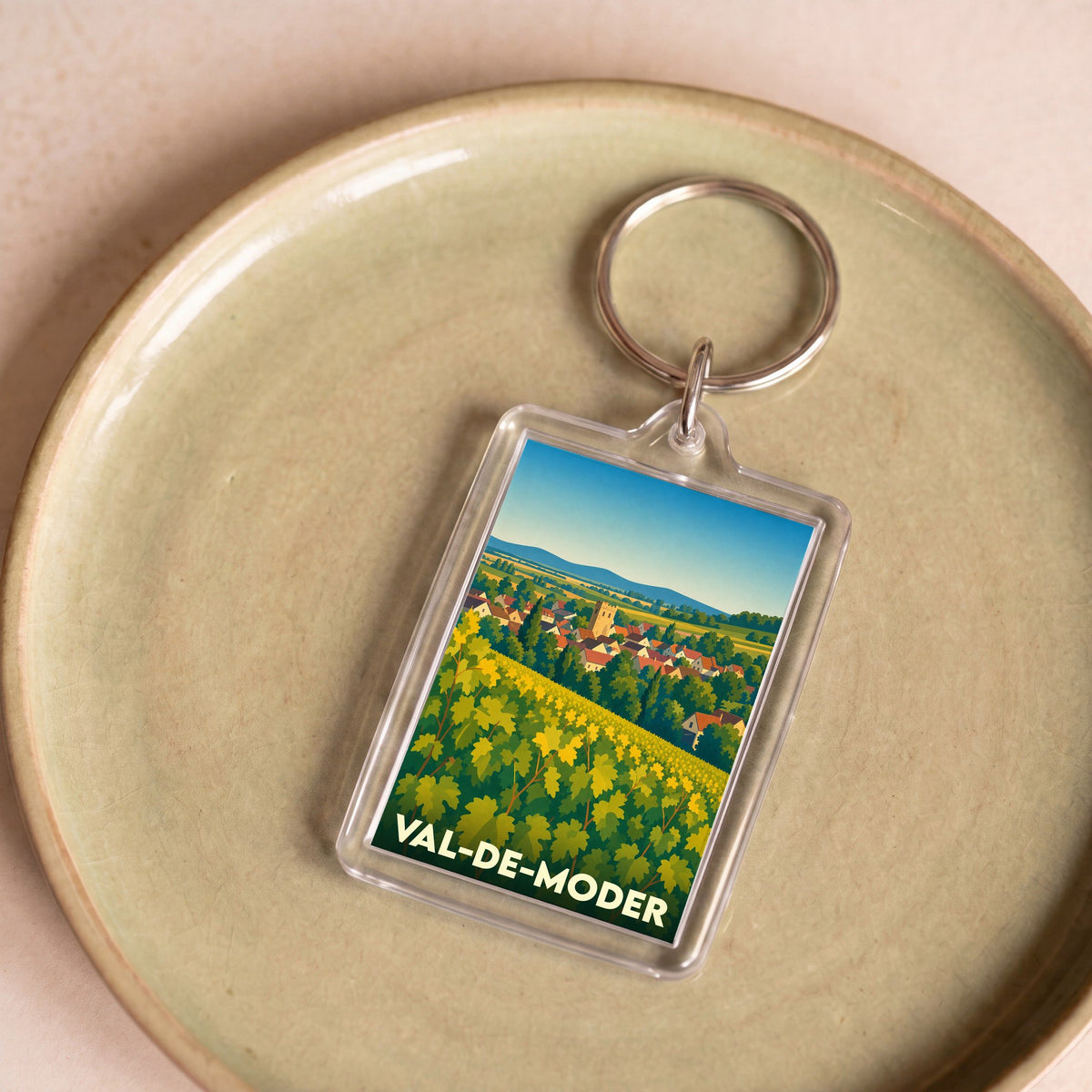 Porte-clés souvenir de la ville de Val-de-Moder avec une illustration stylisée de vignes et du village.