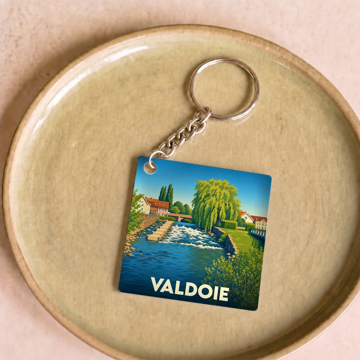 Porte-clés souvenir de la ville de Valdoie avec une illustration stylisée d'un paysage de rivière.