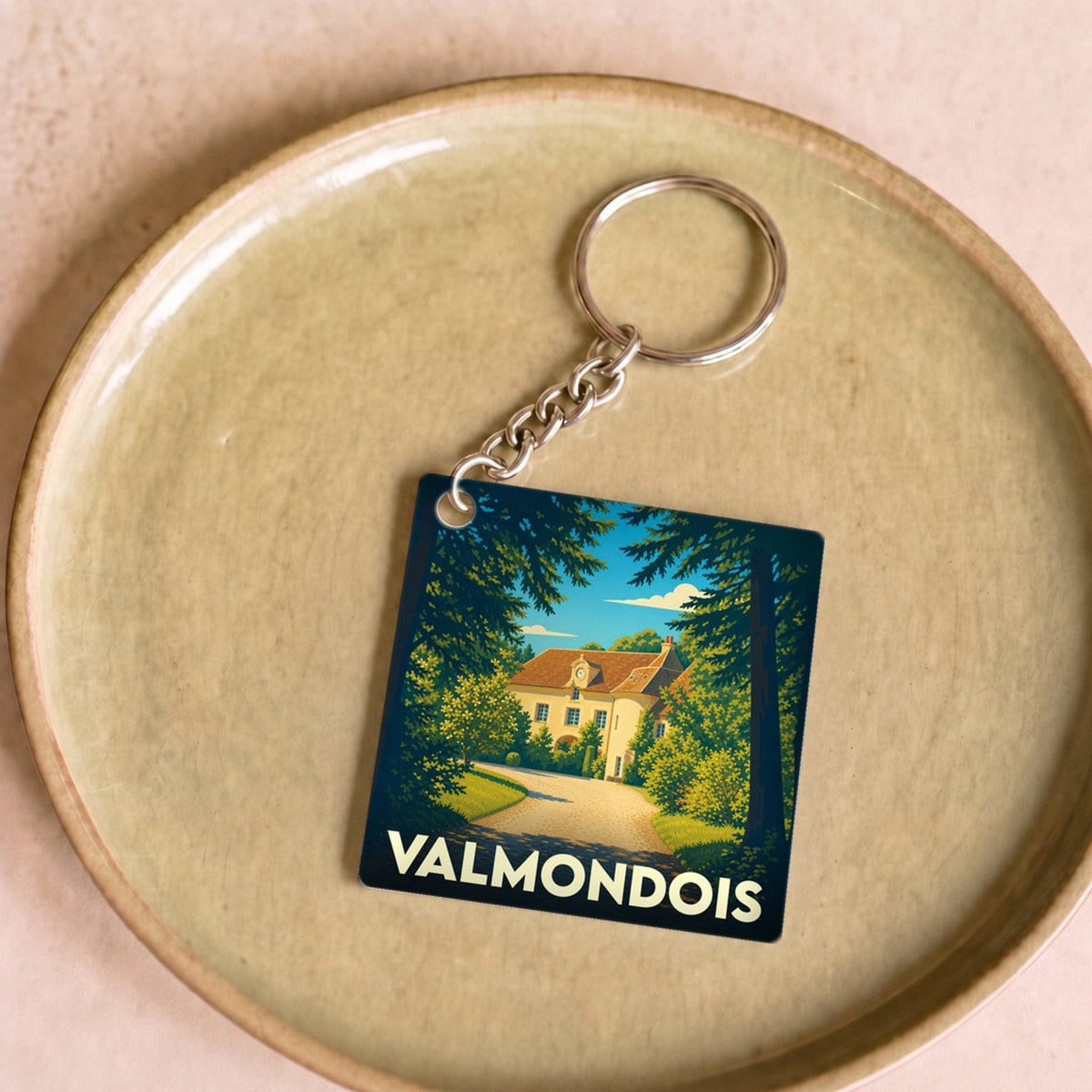 Porte-clés souvenir de la ville de Valmondois avec une illustration stylisée d'un manoir entouré de verdure.