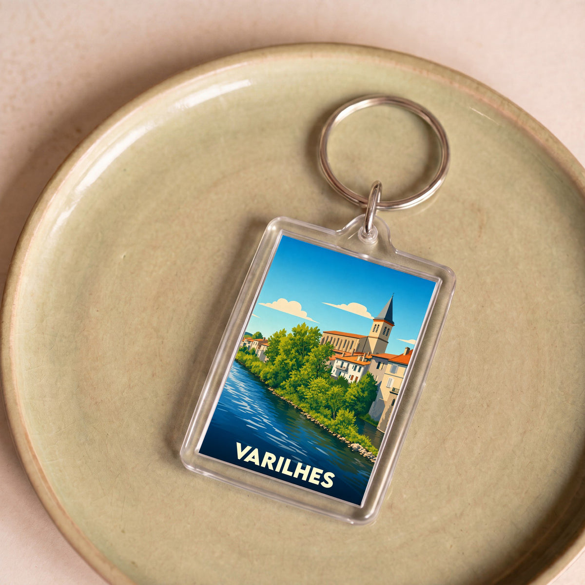 Porte-clés souvenir de la ville de Varilhes avec une illustration stylisée d'un paysage urbain au bord de l'eau.