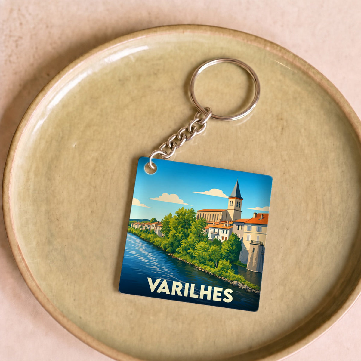 Porte-clés souvenir de la ville de Varilhes avec une illustration stylisée d'un paysage urbain au bord de l'eau.
