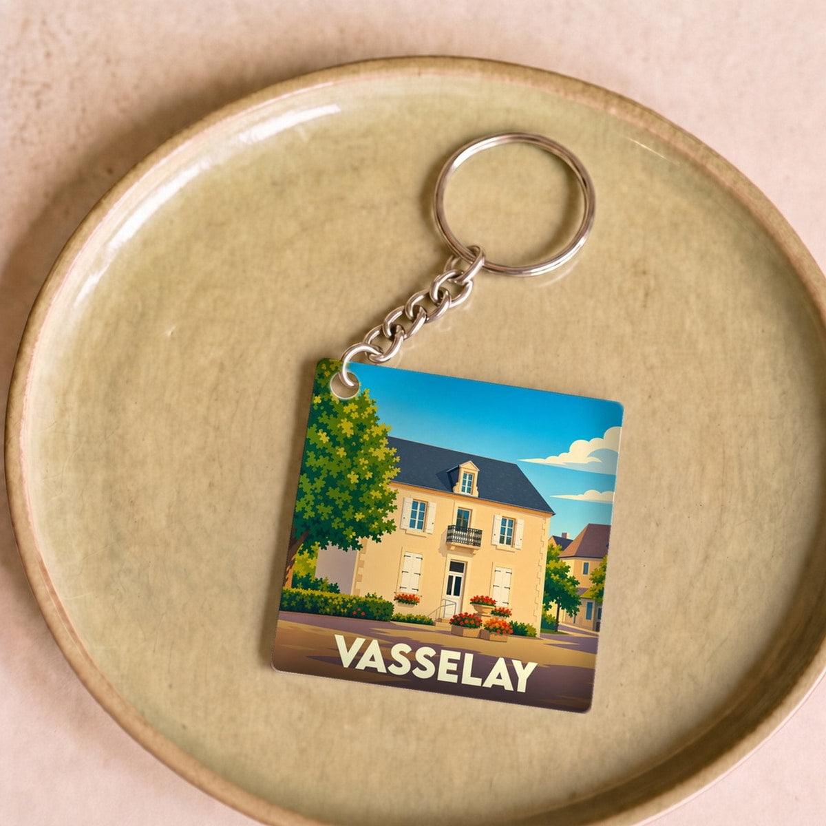 Porte-clés souvenir de la ville de Vasselay avec une illustration stylisée d'une maison de campagne sous un ciel bleu.