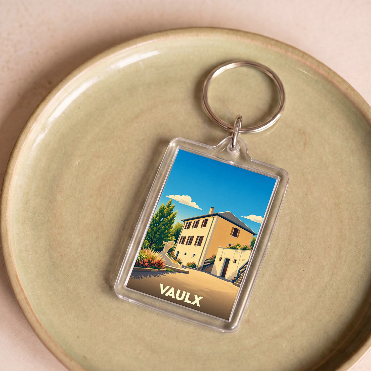 Porte-clés souvenir de la ville de Vaulx avec une illustration stylisée d'une maison ensoleillée.