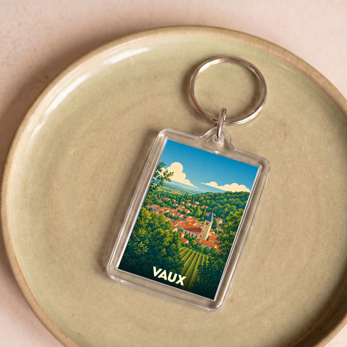 Porte-clés souvenir de la ville de Vaux avec une illustration stylisée d'un village entouré de verdure.