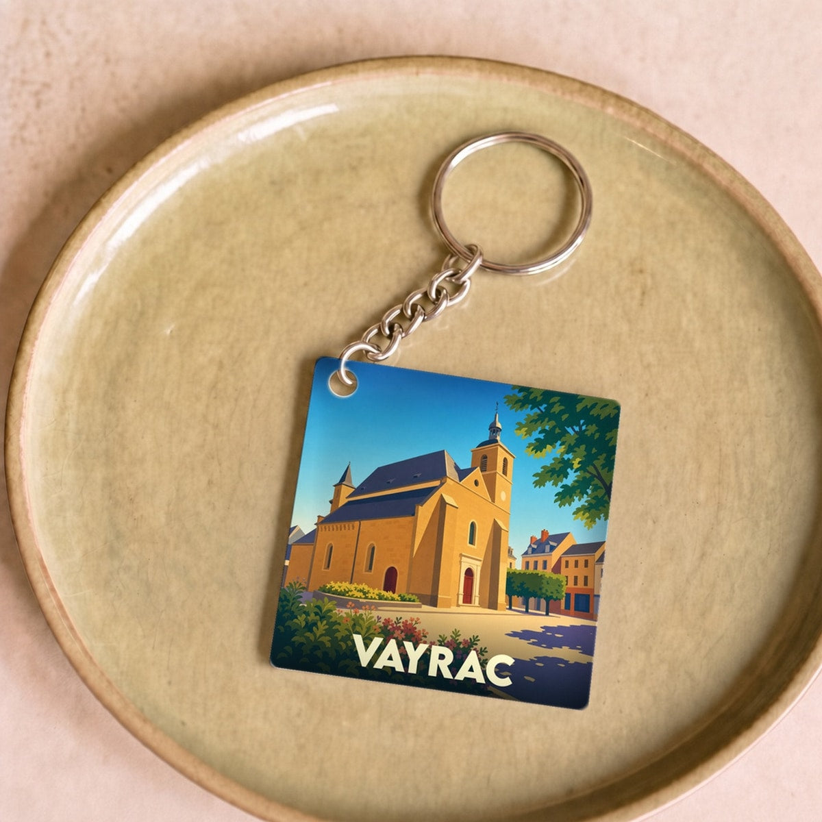 Porte-clés souvenir de la ville de Vayrac avec une illustration stylisée de son église sous un ciel bleu.