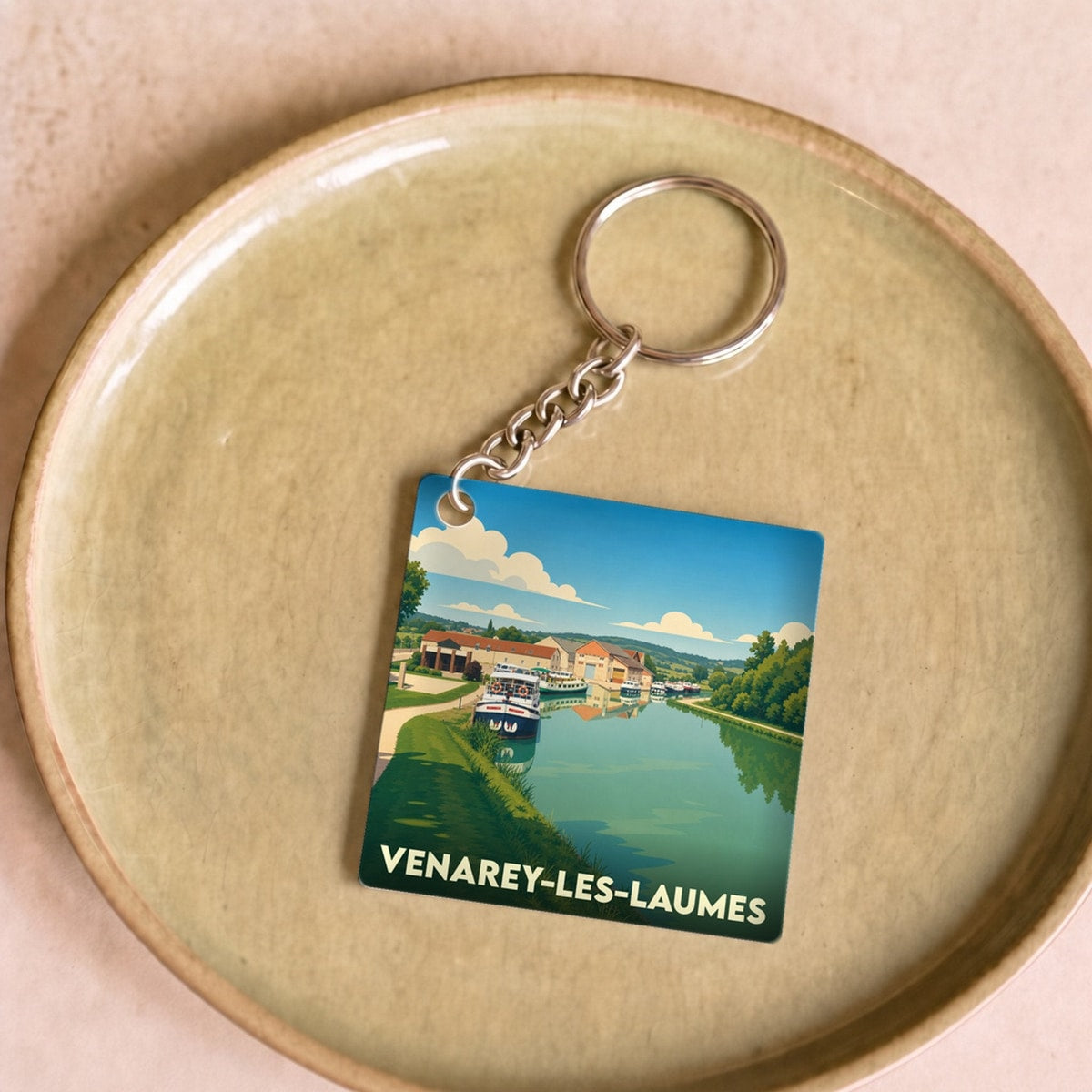 Porte-clés souvenir de la ville de Venarey-les-Laumes avec une illustration stylisée d'un canal et de bateaux.
