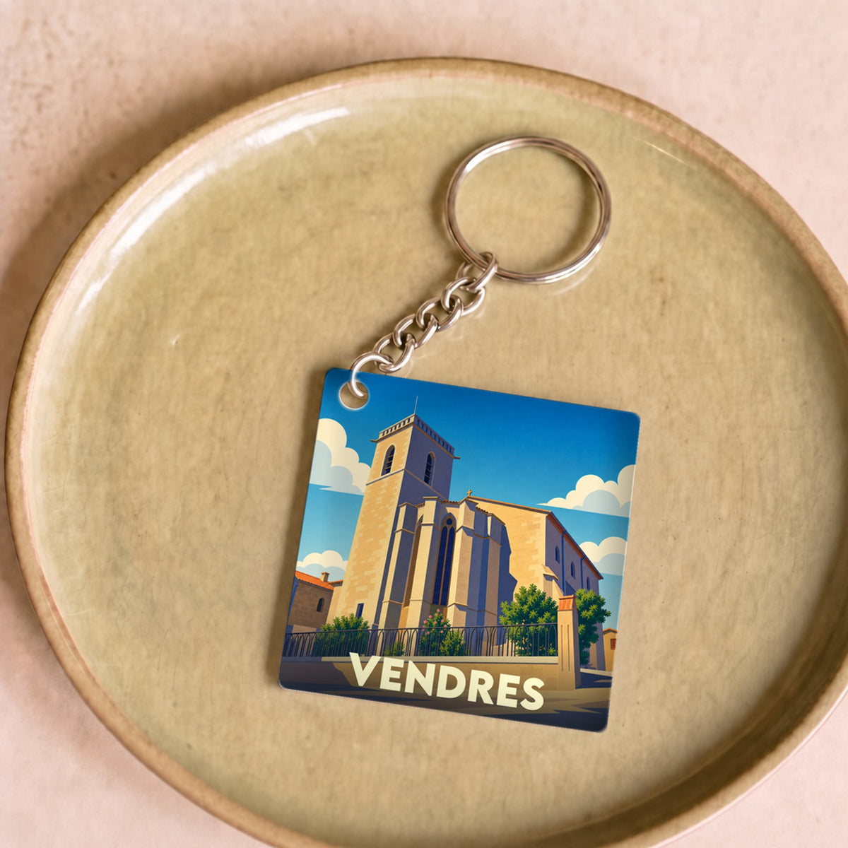 Porte-clés souvenir de la ville de Vendres avec une illustration stylisée de son église sous un ciel bleu.