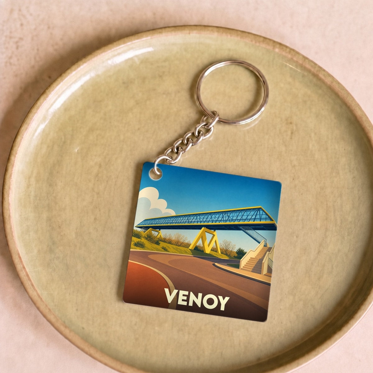 Porte-clés souvenir de la ville de Venoy avec une illustration stylisée d'une passerelle.