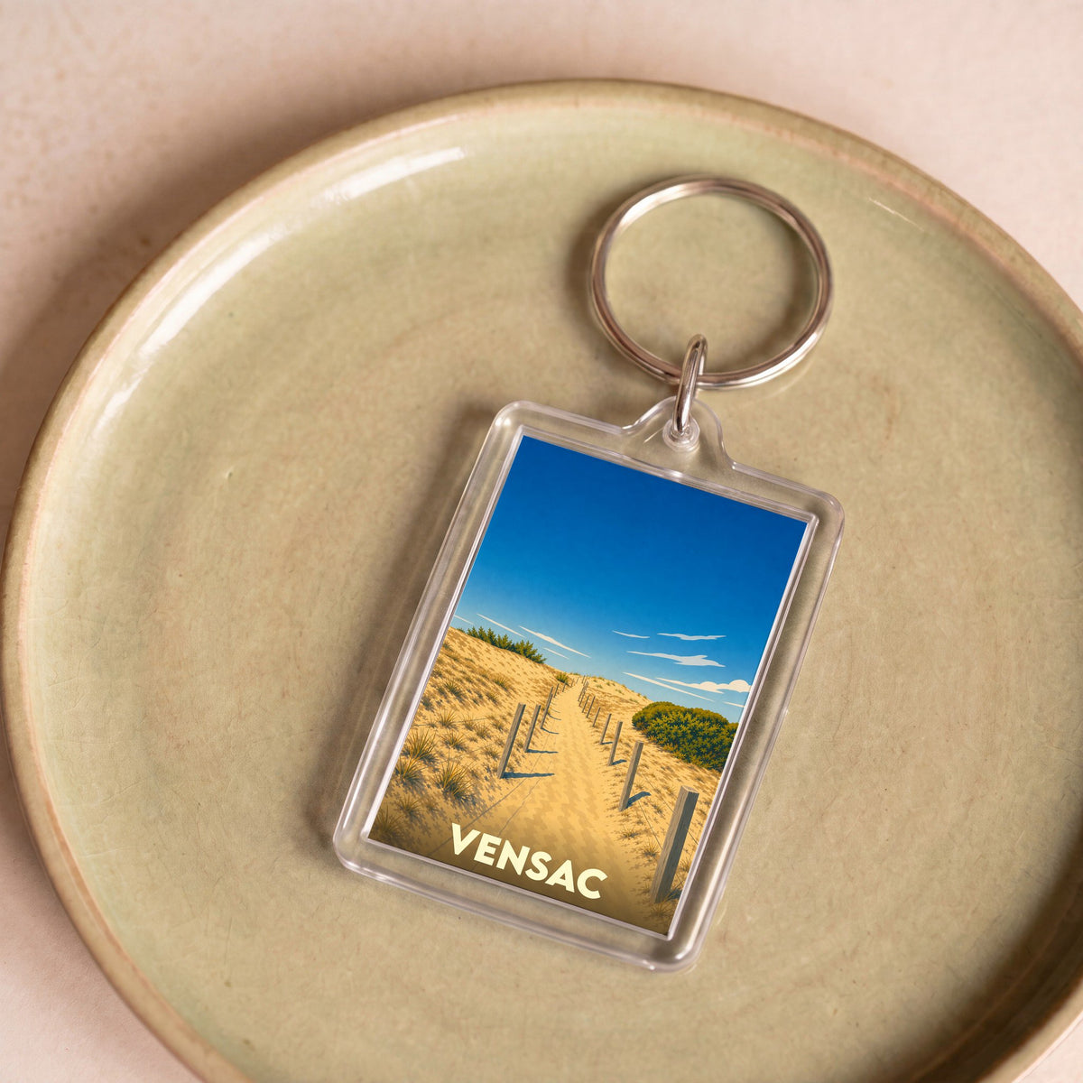 Porte-clés souvenir de la ville de Vensac avec une illustration stylisée d'un chemin à travers les dunes.