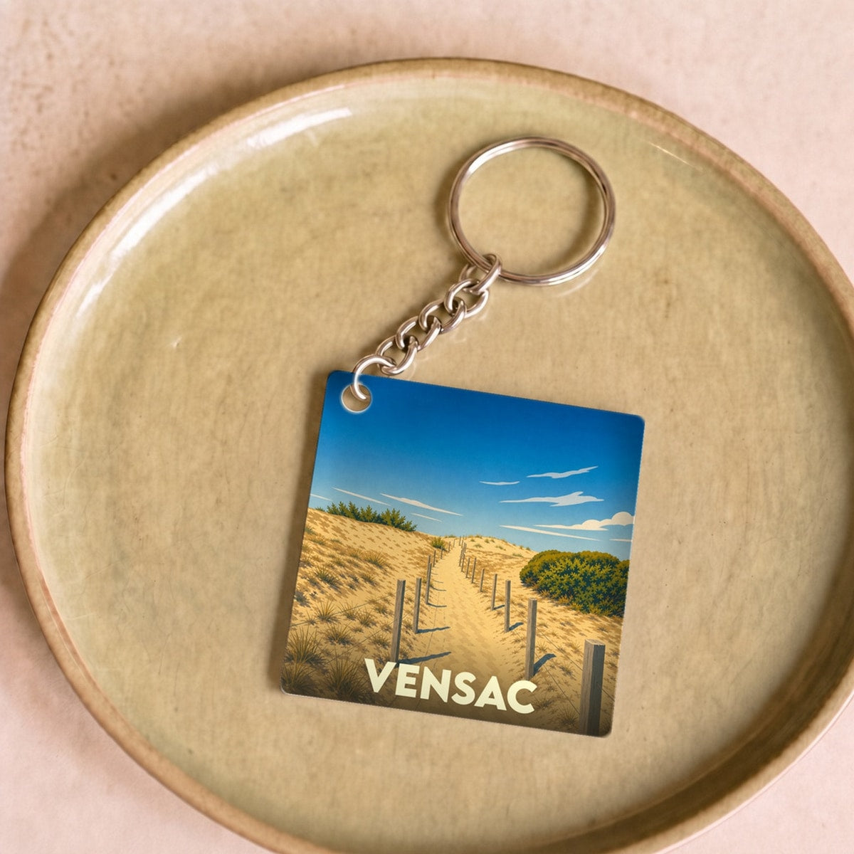 Porte-clés souvenir de la ville de Vensac avec une illustration stylisée d'un chemin à travers les dunes.