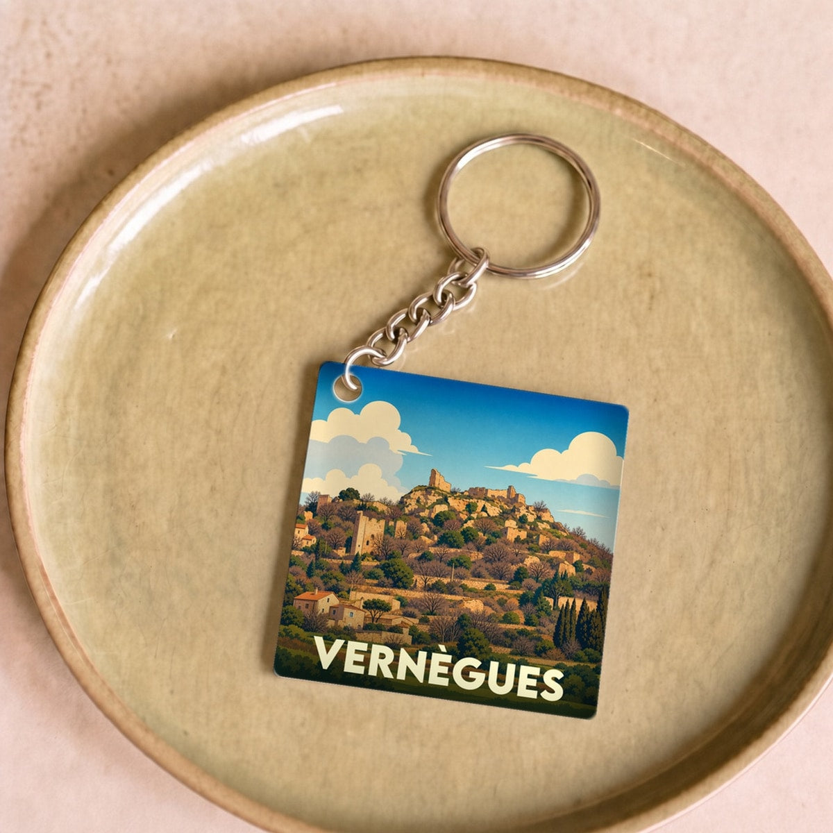 Porte-clés souvenir de la ville de Vernègues avec une illustration stylisée d'un village perché sous un ciel azur.