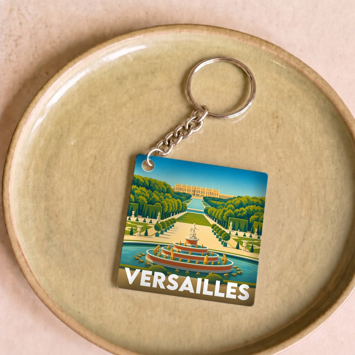 Porte-clés souvenir de la ville de Versailles avec une illustration stylisée de son château et de ses jardins.