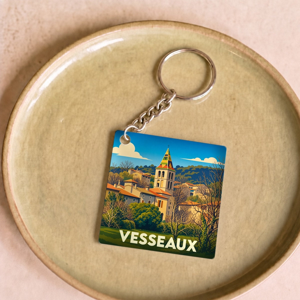 Porte-clés souvenir de la ville de Vesseaux avec une illustration stylisée de son église et de ses paysages.