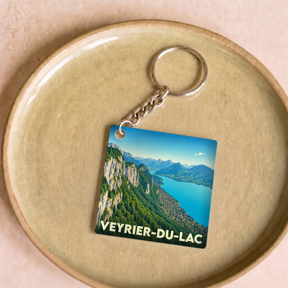 Porte-clés souvenir de la ville de Veyrier-du-Lac avec une illustration stylisée d'un paysage montagneux bordant le lac.