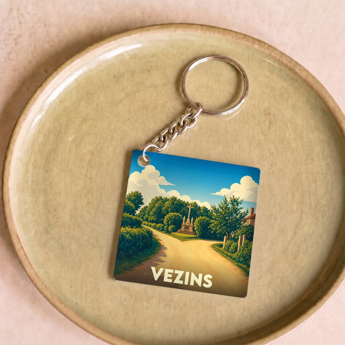Porte-clés souvenir de la ville de Vezins avec une illustration stylisée d'un chemin de campagne.