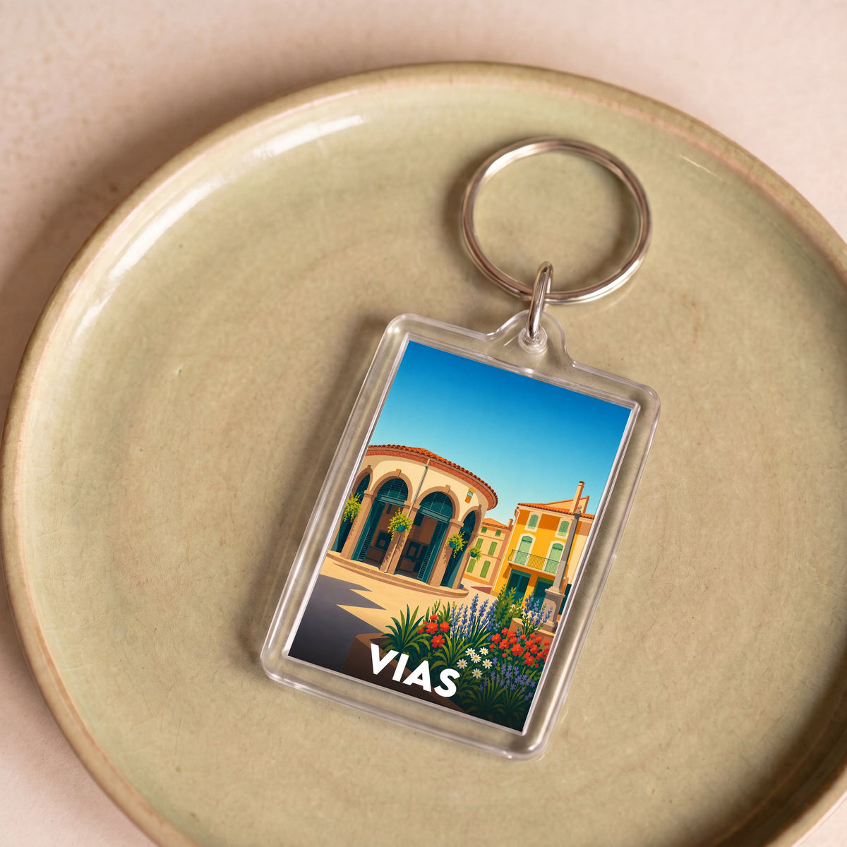 Porte-clés souvenir de la ville de Vias avec une illustration stylisée et colorée.