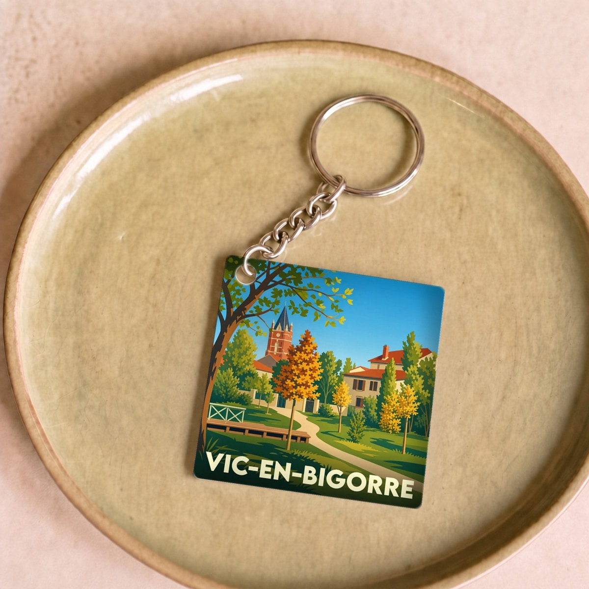 Porte-clés souvenir de la ville de Vic-en-Bigorre avec une illustration stylisée d'un parc et d'un clocher.