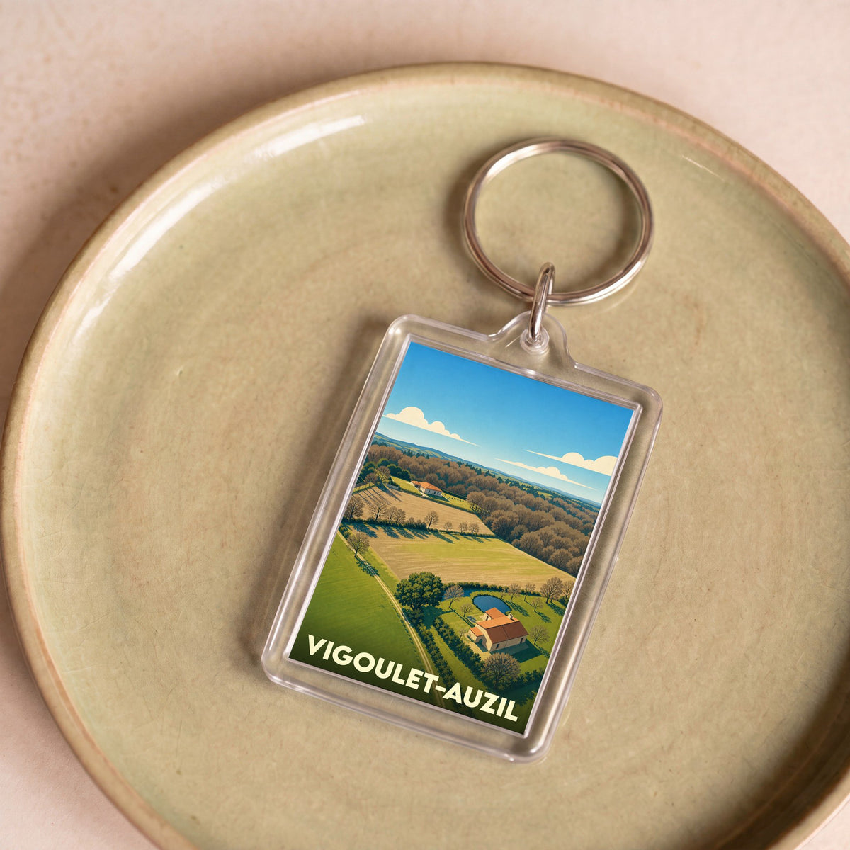 Porte-clés souvenir de la ville de Vigoulet-Auzil avec une illustration stylisée de paysages vallonnés.
