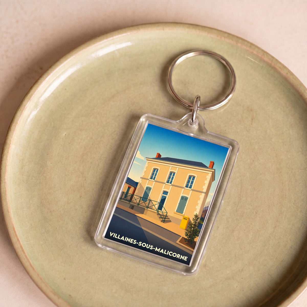 Porte-clés souvenir de la ville de Villaines-sous-Malicorne avec une illustration stylisée d'un bâtiment typique.