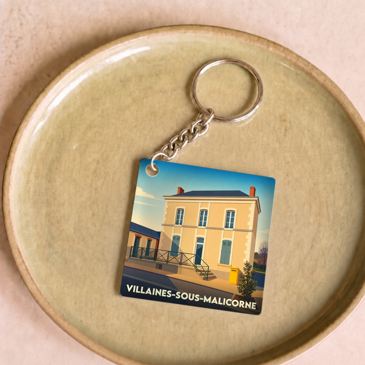 Porte-clés souvenir de la ville de Villaines-sous-Malicorne avec une illustration stylisée d'un bâtiment typique.
