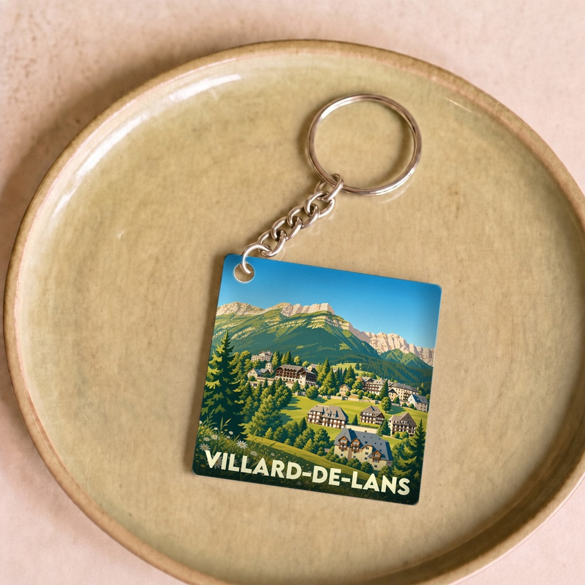 Porte-clés souvenir de la ville de Villard-de-Lans illustrant un paysage de montagne stylisé.