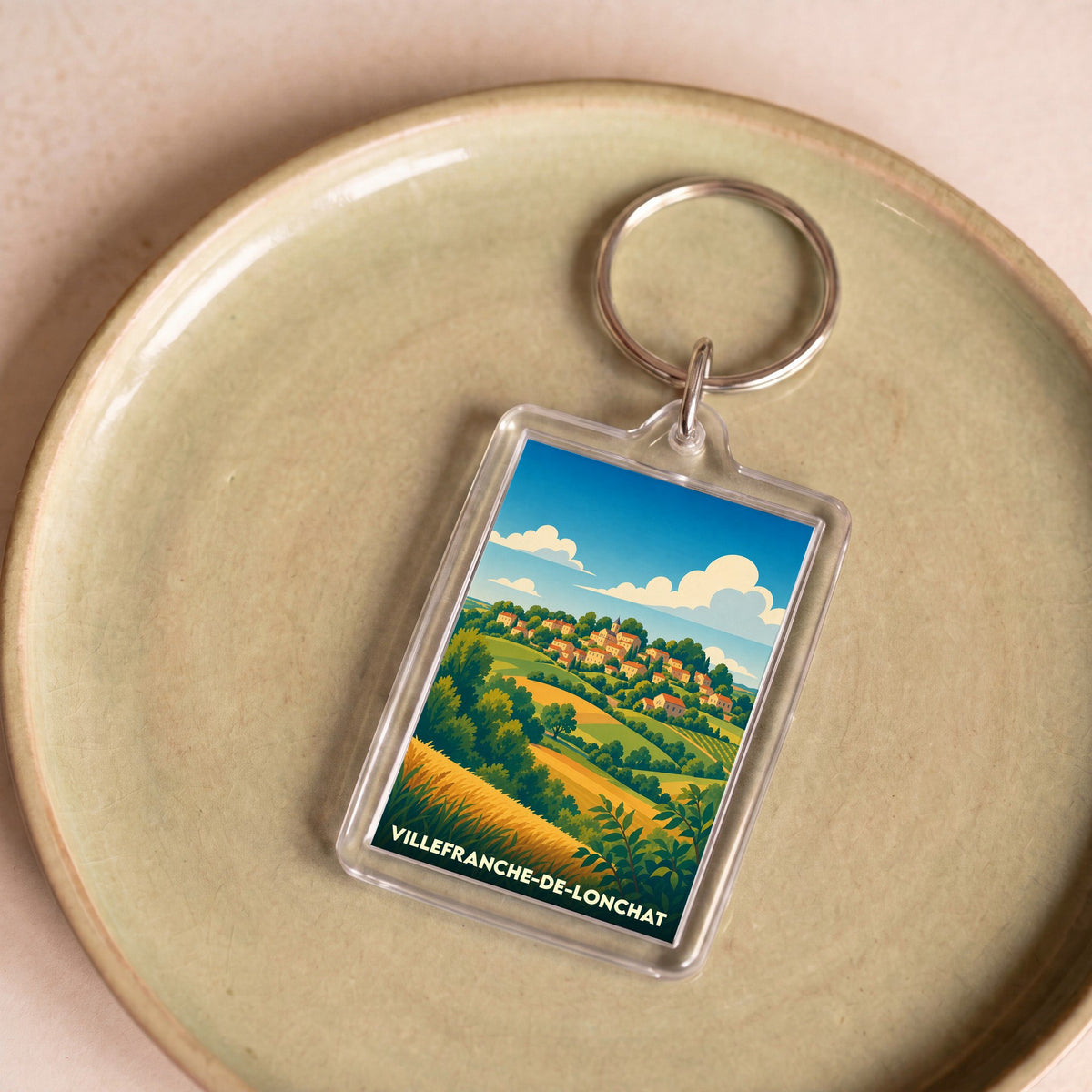 Porte-clés souvenir de la ville de Villefranche-de-Lonchat avec une illustration de paysage champêtre.