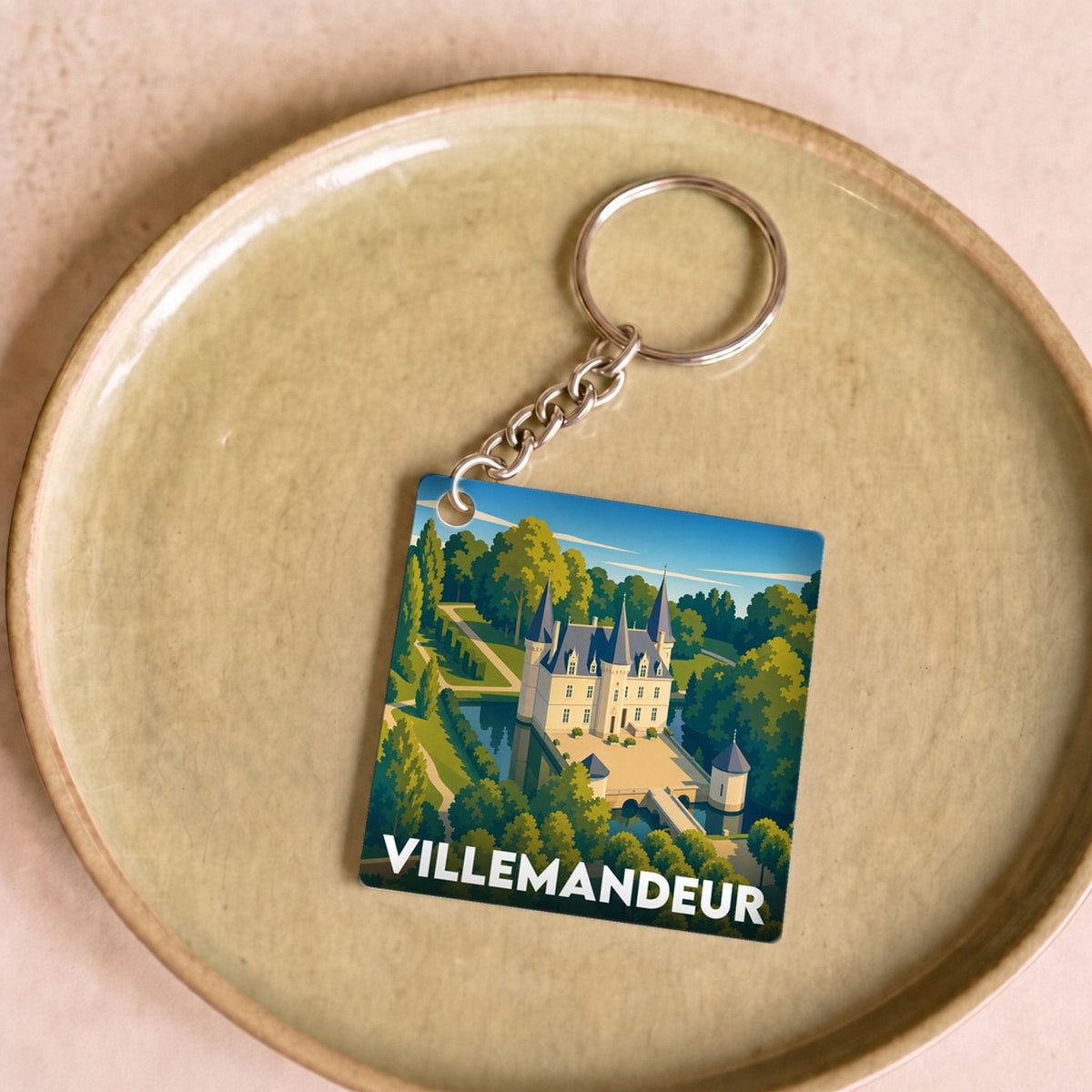 Porte-clés souvenir de la ville de Villemandeur avec une illustration stylisée d'un château entouré de verdure.