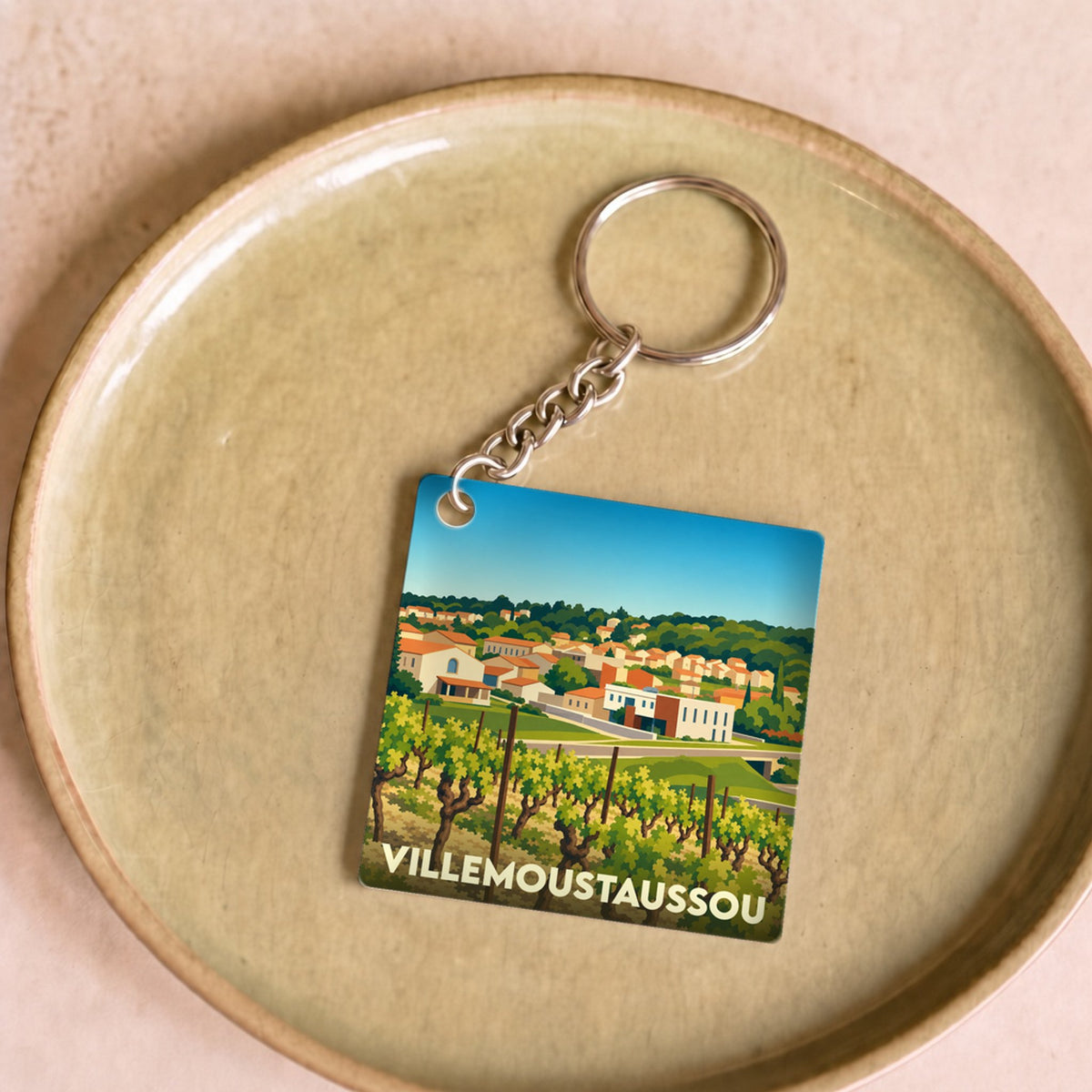 Porte-clés souvenir de la ville de Villemoustaussou avec une illustration stylisée de vignes et du village.