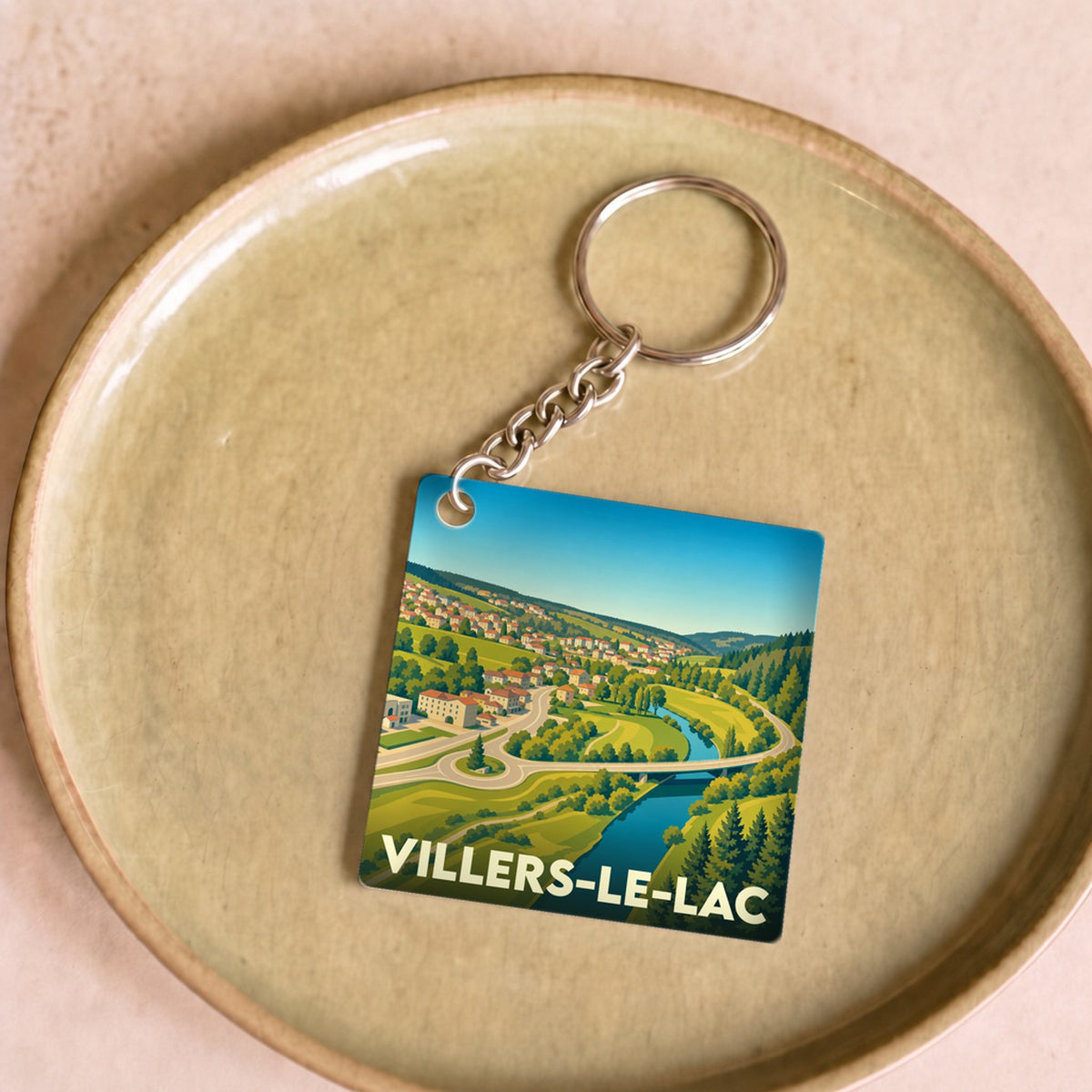 Porte-clés souvenir de la ville de Villers-le-Lac avec une illustration stylisée d'un paysage de vallée.