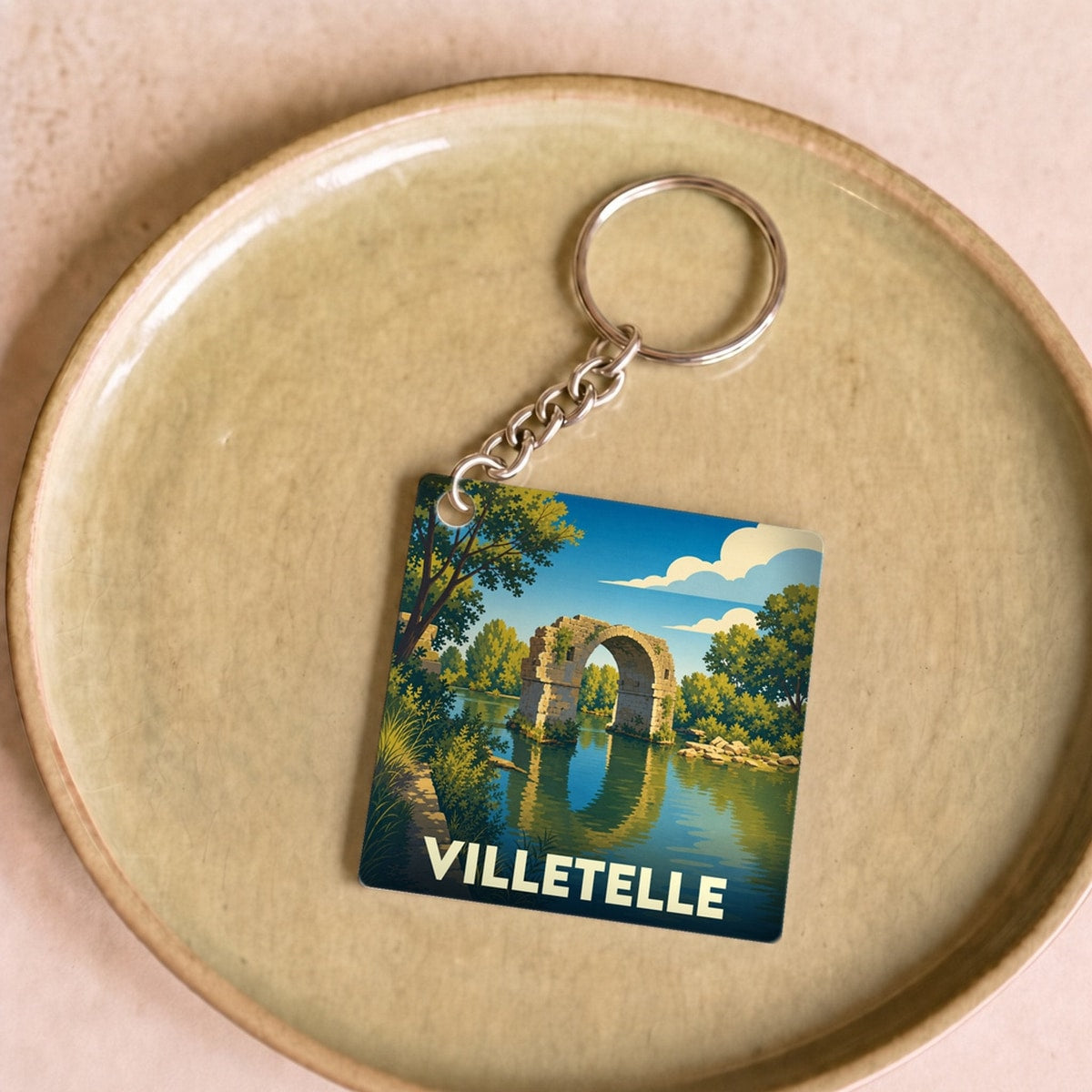Porte-clés souvenir de la ville de Villetelle avec une illustration stylisée d'un pont historique au bord de l'eau.