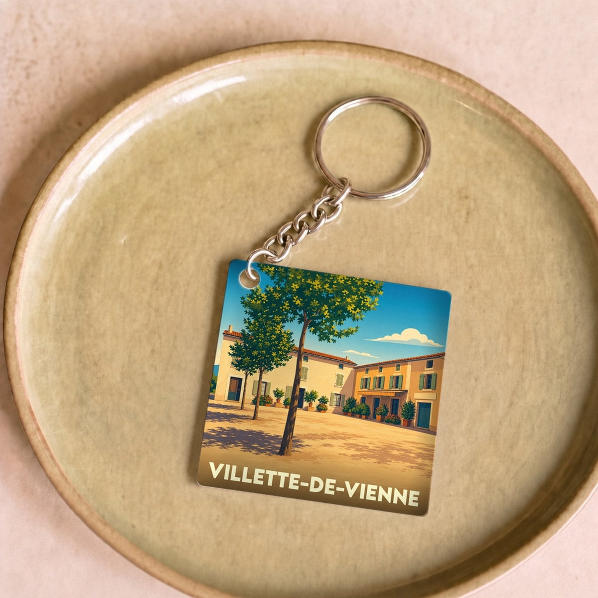 Porte-clés souvenir de la ville de Villette-de-Vienne avec une illustration stylisée d'une place ensoleillée.