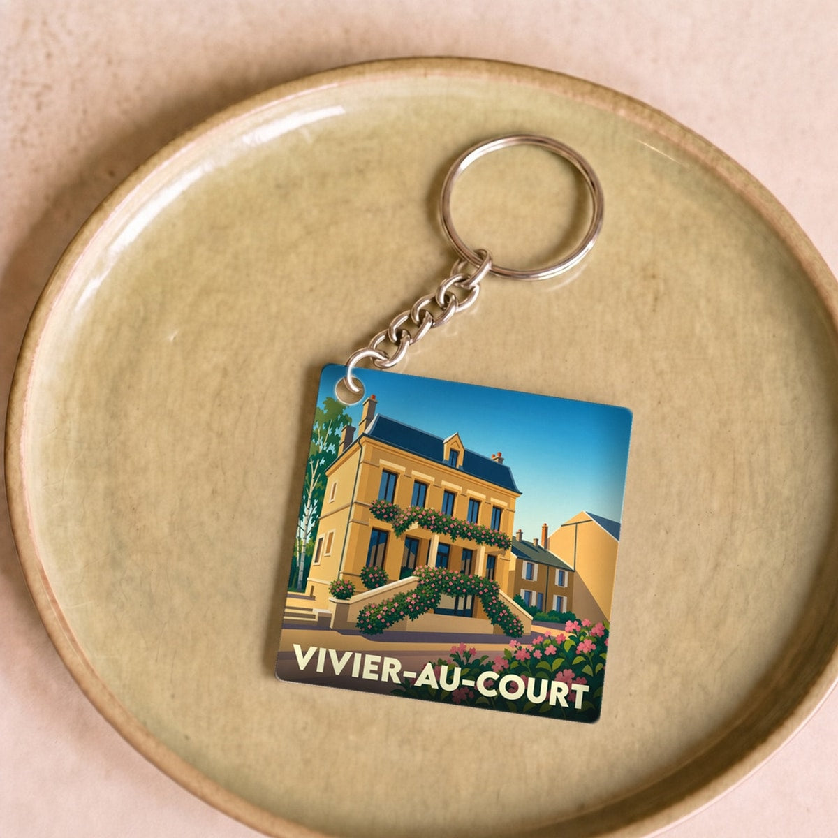 Porte-clés souvenir de la ville de Vivier-au-Court avec une illustration stylisée d'une maison fleurie.