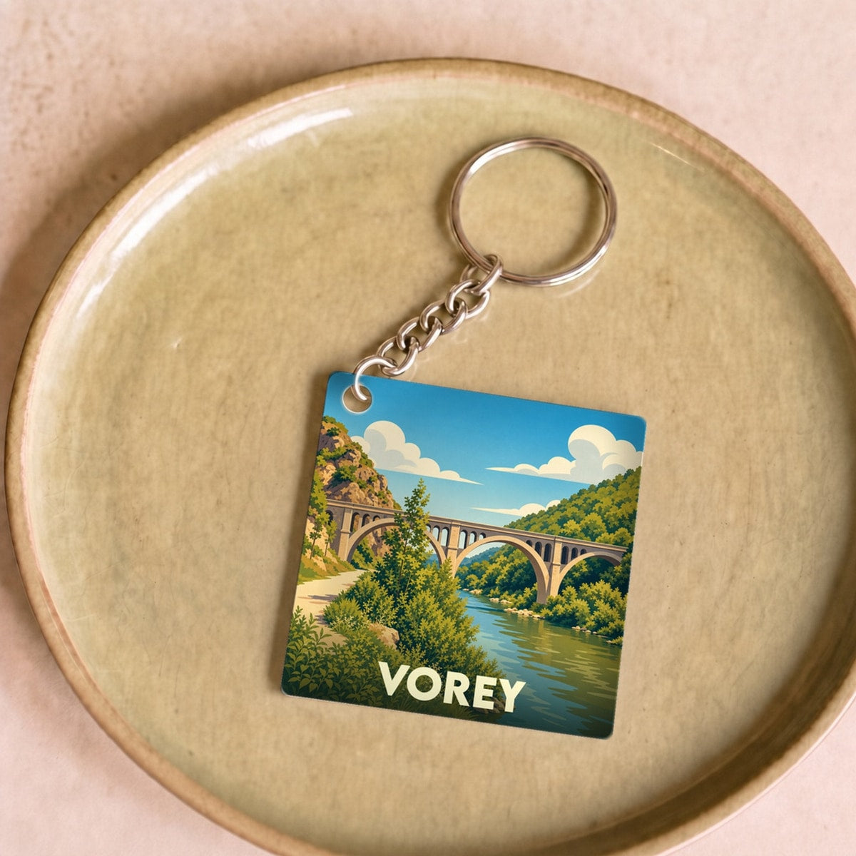 Porte-clés souvenir de la ville de Vorey avec une illustration stylisée d'un pont enjambant une rivière.