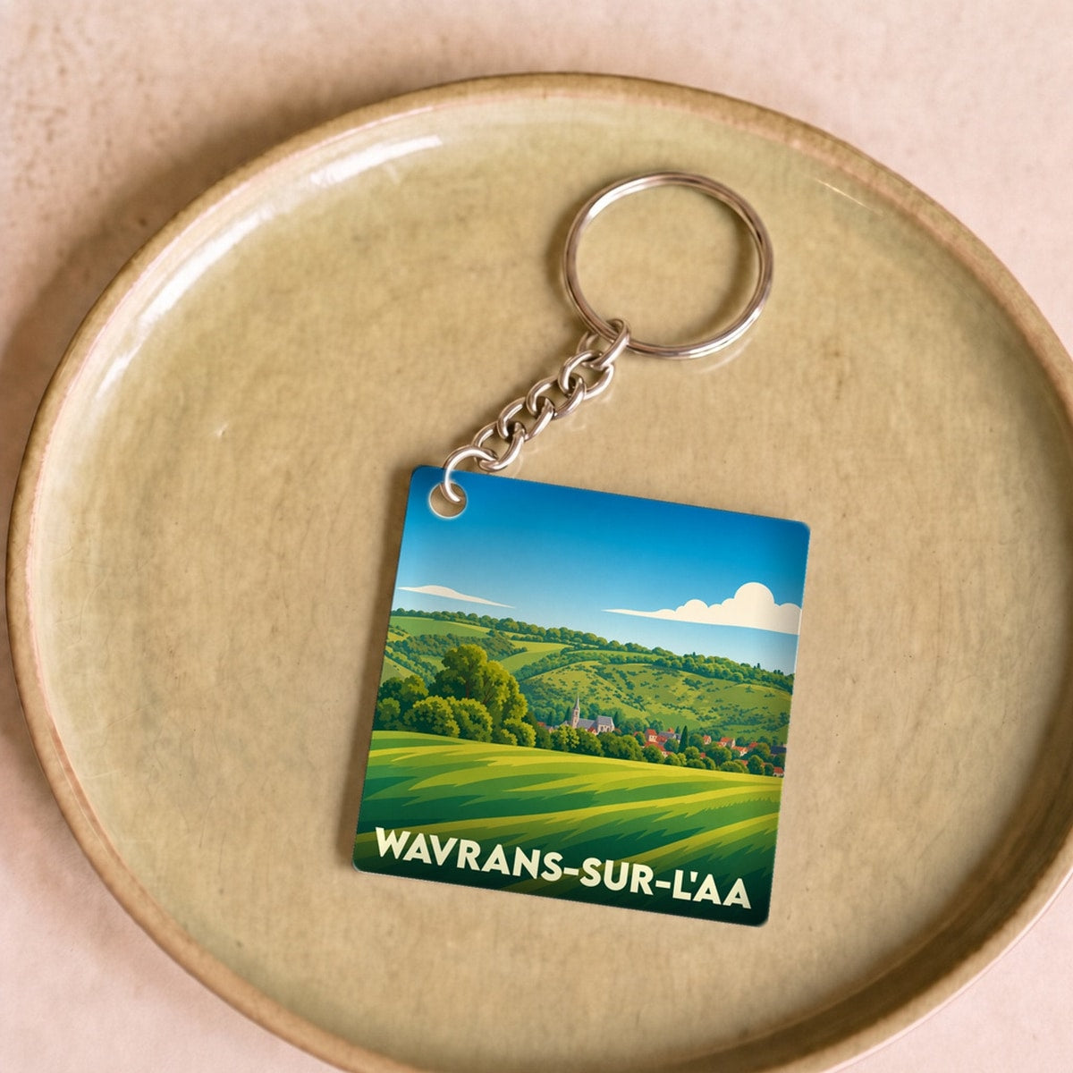 Porte-clés souvenir de la ville de Wavrans-sur-l'Aa avec une illustration stylisée de paysages vallonnés.