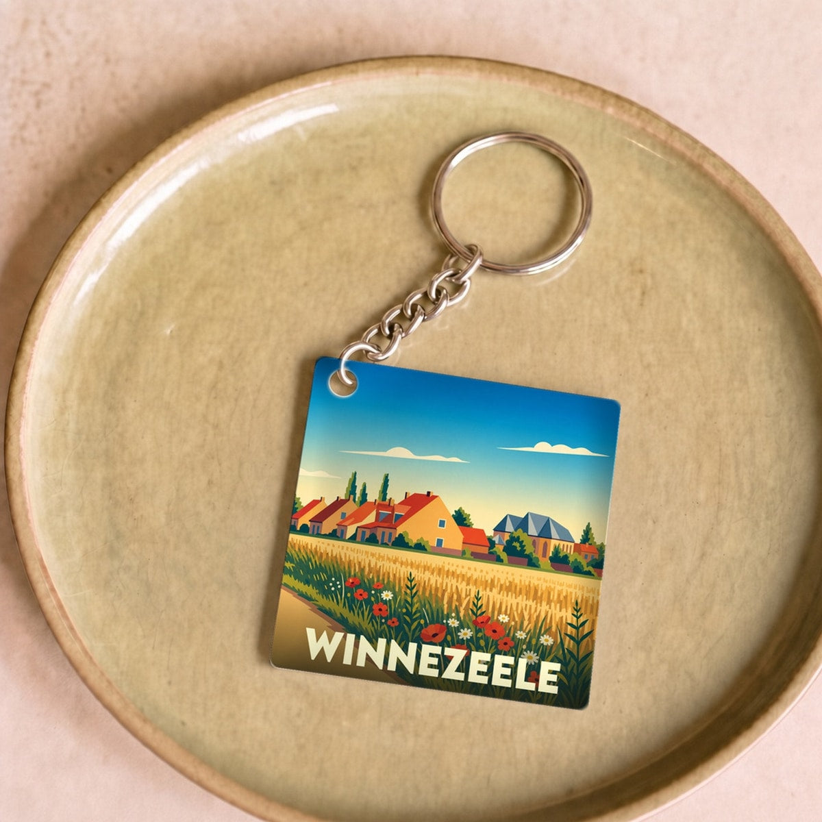 Porte-clés souvenir de la ville de Winnezeele avec une illustration stylisée d'un paysage de campagne.