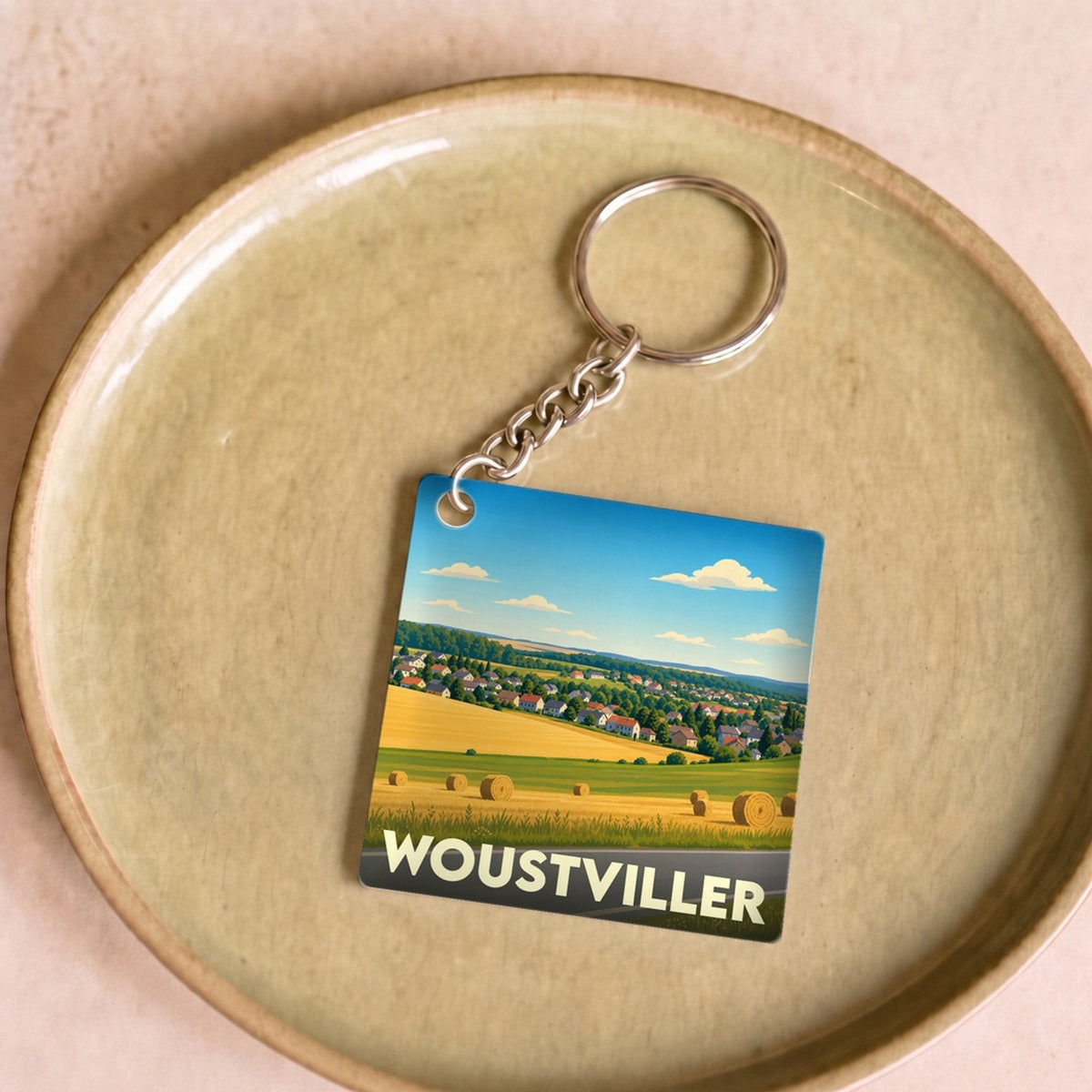 Porte-clés souvenir de la ville de Woustviller avec une illustration stylisée de paysages ruraux.
